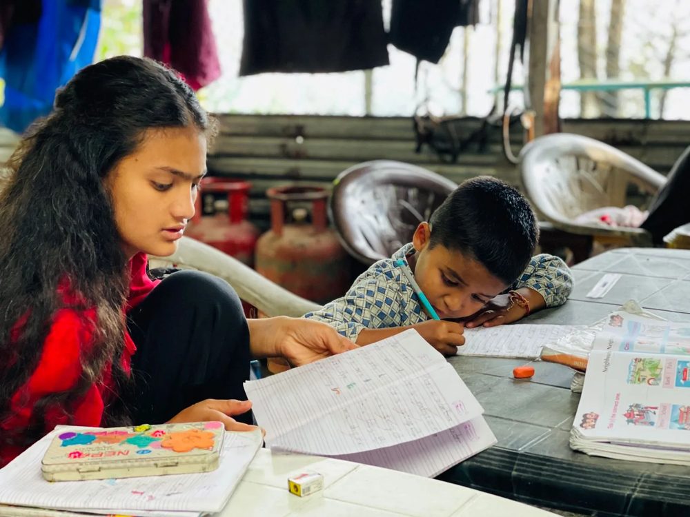 An older girl at the home going through an exercise book with a younger boy, helping him with his handwriting.